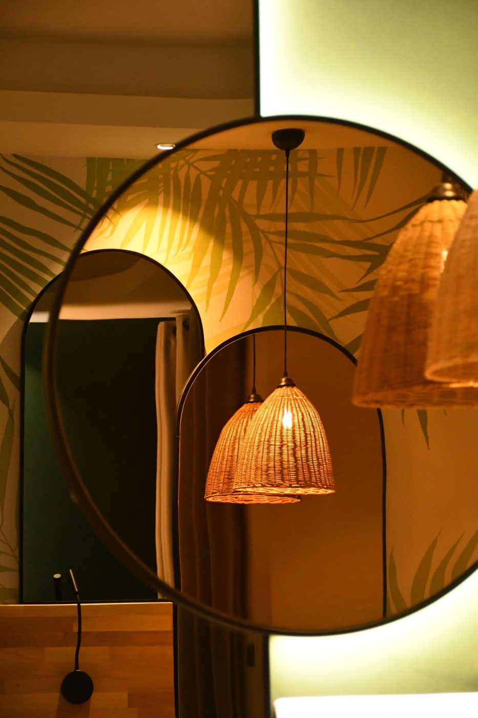 Jeu de miroirs ronds et en arche reflétant des suspensions en rotin devant un papier peint à palmes